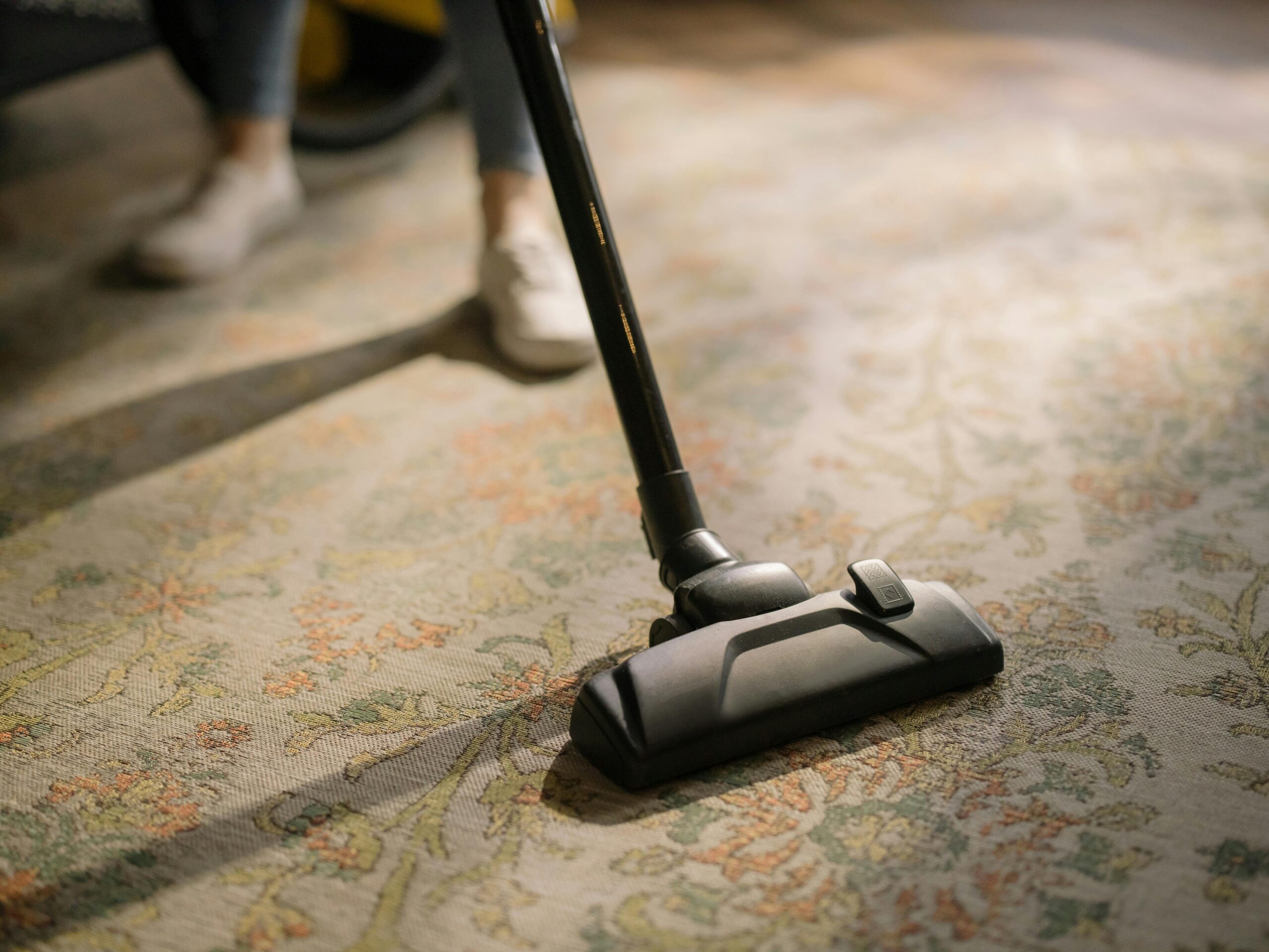 A professional cleaner in red coveralls vacuuming a modern living room with a yellow vacuum cleaner.