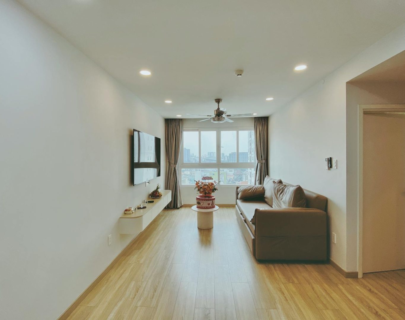 Spacious living room featuring modern decor, cozy sofa, and large city view window.