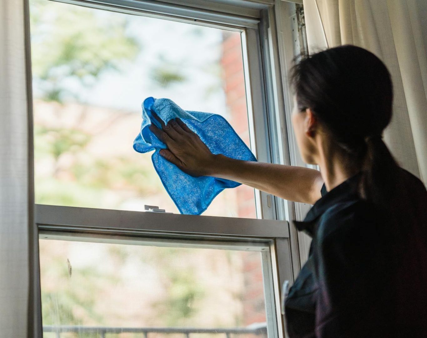 A woman cleans a window using a blue microfiber cloth providing a streak-free shine.