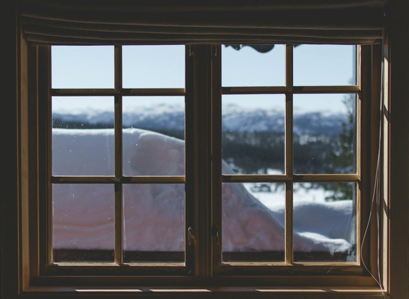 A scenic view of snow-capped mountains through a wooden window frame, capturing the serene winter landscape.